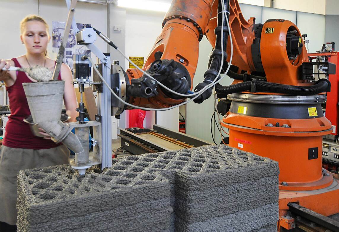 An der Versuchsanlage für additive Fertigung wird durch Extrusion von Holzleichtbeton ein Wandelement hergestellt. Studentin Bettina Saile befüllt den Versuchsextruder mit Frischbeton. (Foto © K. Henke / TUM);